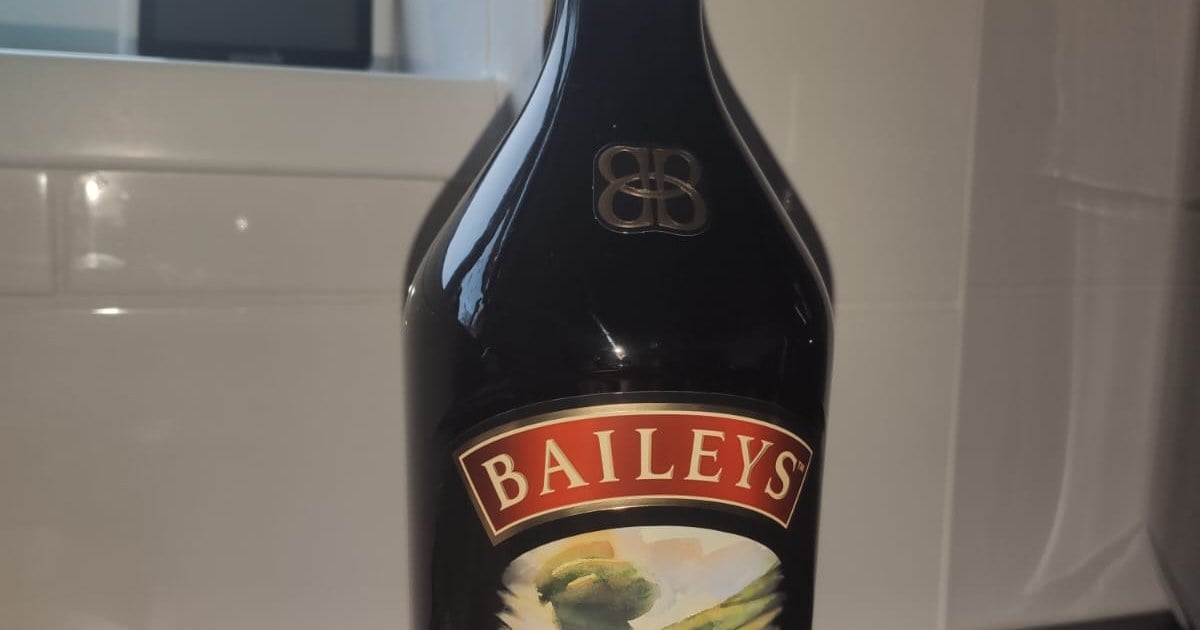 A bottle of Baileys Irish Cream on a kitchen counter, showing its brown glass, gold BB emblem and red BAILEYS label