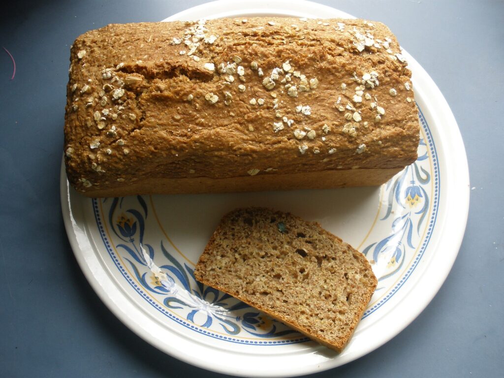 A loaf of Irish brown soda bread topped with rolled oats, sliced open on a patterned plate