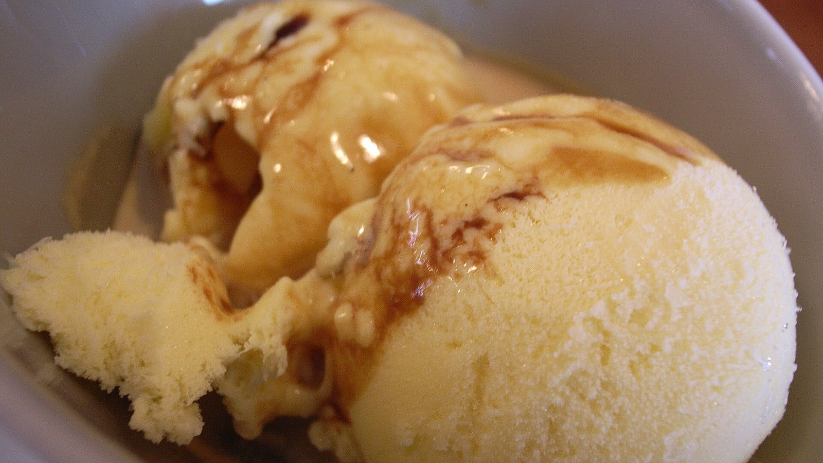 Two scoops of gelato drizzled with caramel sauce in a white bowl