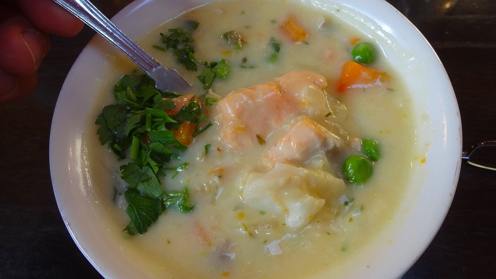 A bowl of seafood chowder with shrimp, fish, peas and parsley