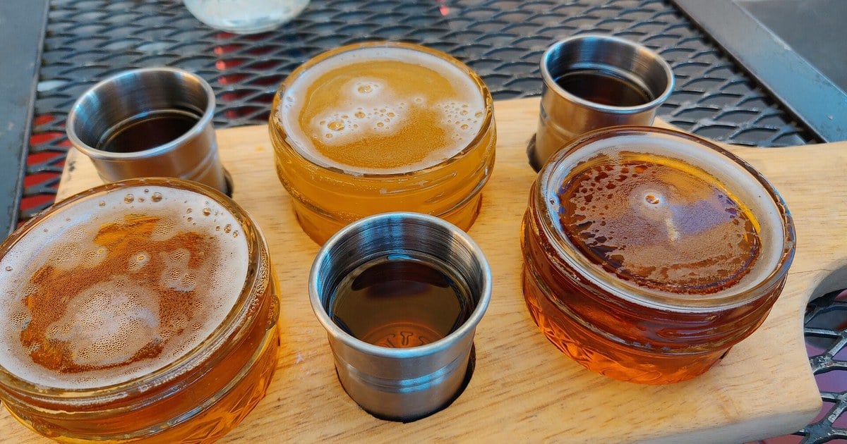 A tasting flight of Irish whiskey samples served in glass jars and steel cups on a wooden board
