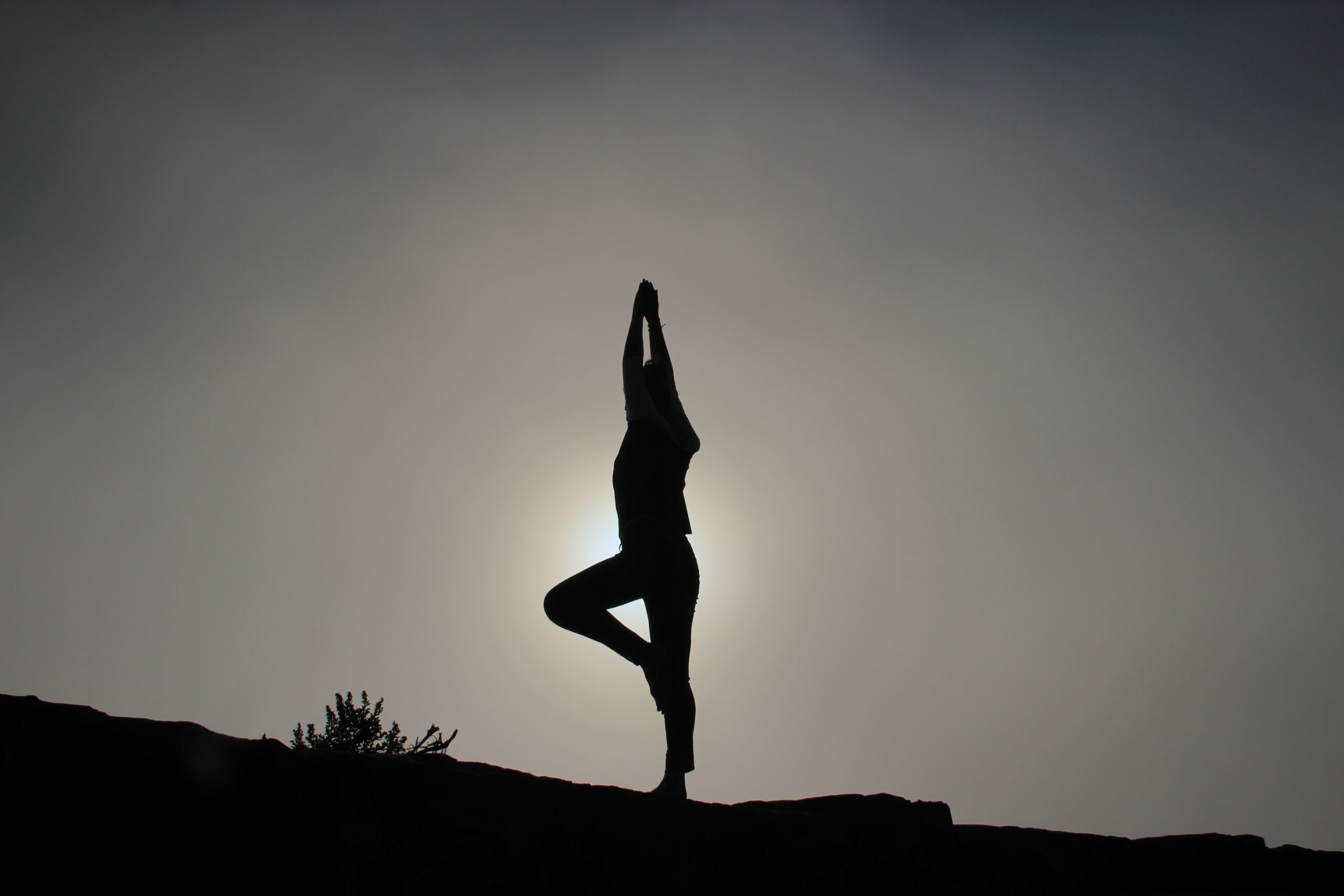 Silhouette of a woman practicing yoga tree pose outdoors at sunrise