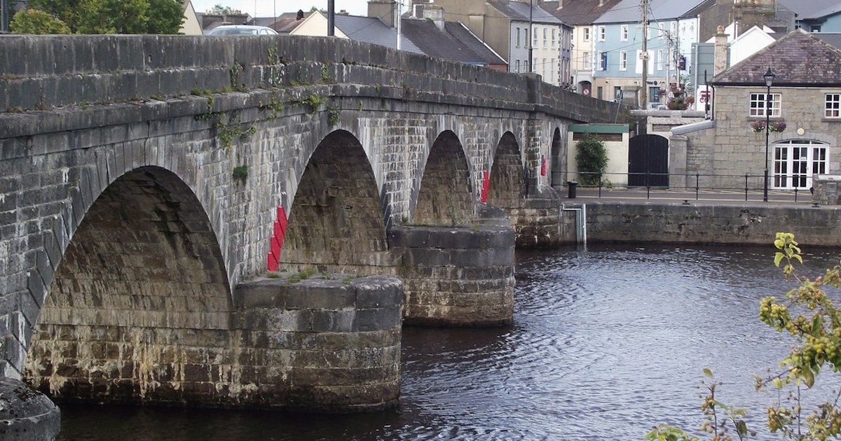 Stone arched bridge over a river in an Irish town, framed by colourful shopfronts