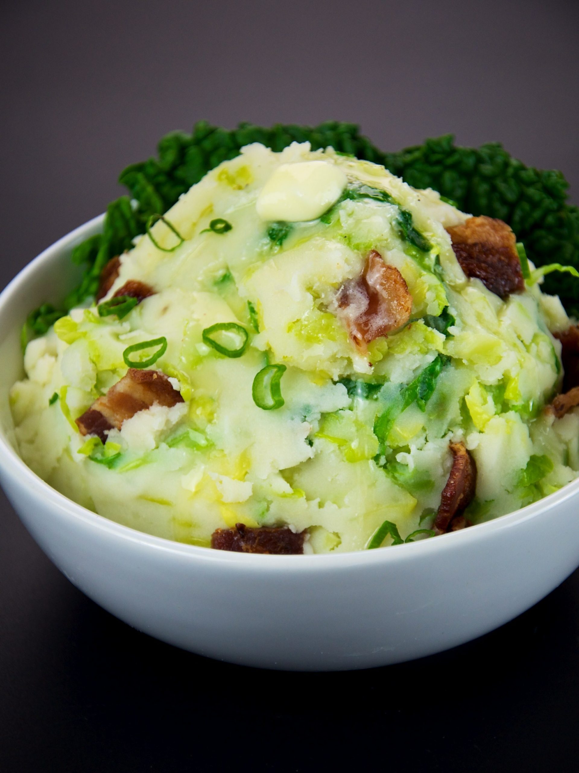 A bowl of colcannon: creamy mashed potato mixed with kale, spring onions and crispy bacon, topped with a knob of melting butter