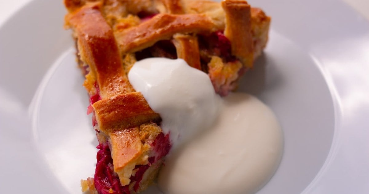 Slice of Irish rhubarb tart with a lattice pastry crust and softly whipped cream on a white plate