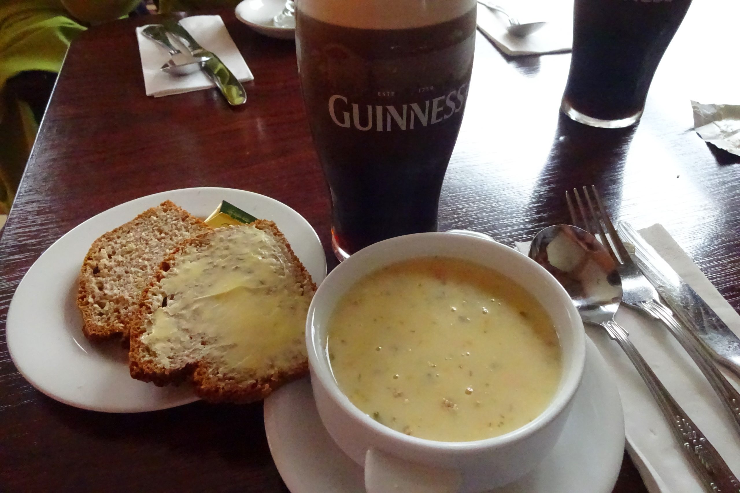 Bowl of creamy Irish seafood chowder with brown bread and butter on the side, and a pint of Guinness on an Irish pub table