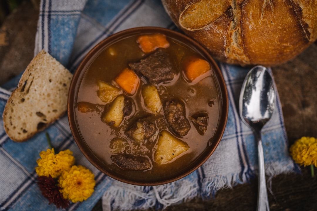 Bowl of Irish beef stew with carrots and potatoes, served with crusty bread and a spoon on a blue plaid cloth