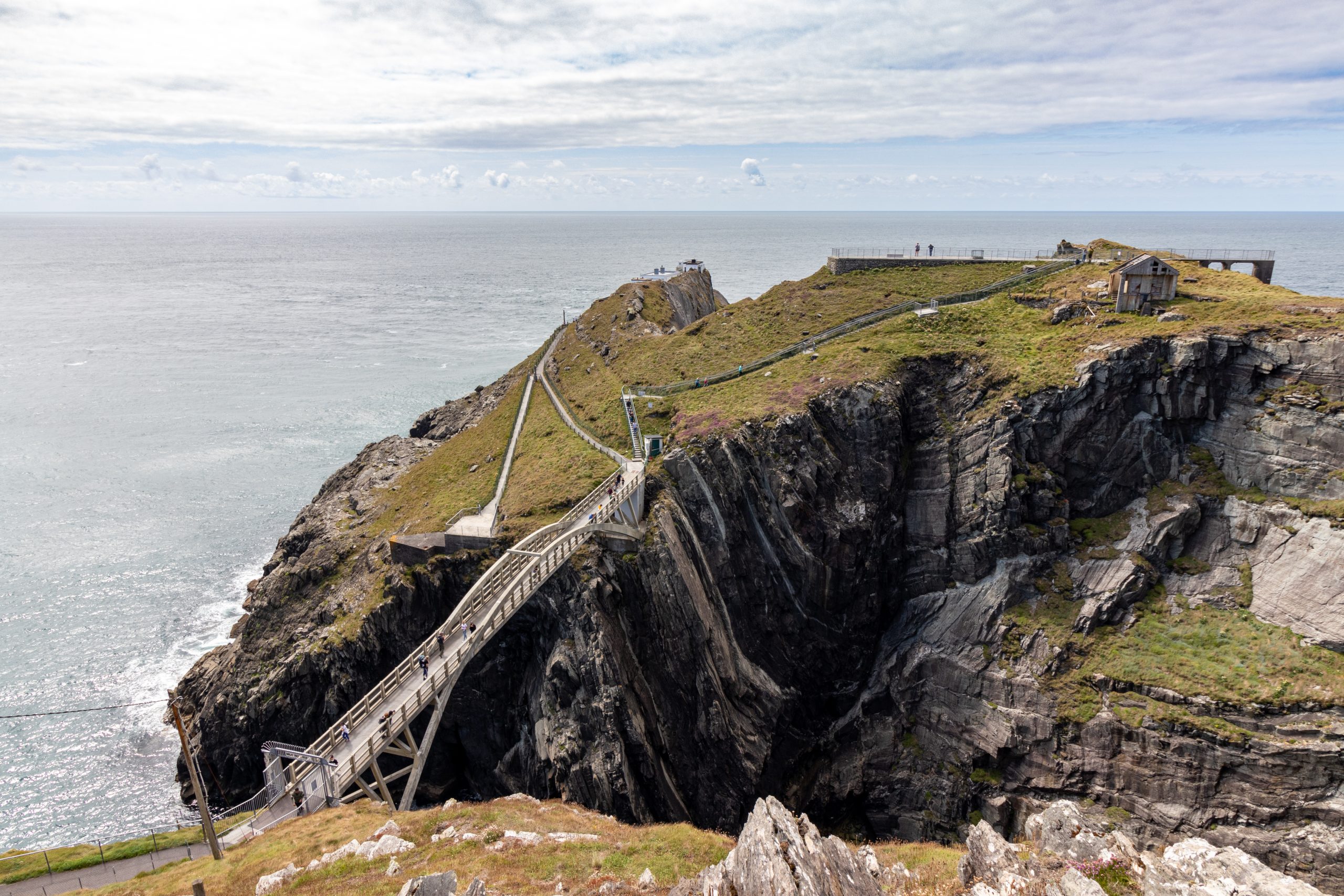 Footbridge crossing a chasm in the sea cliffs at Mizen Head, County Cork, with the signal station on the headland beyond