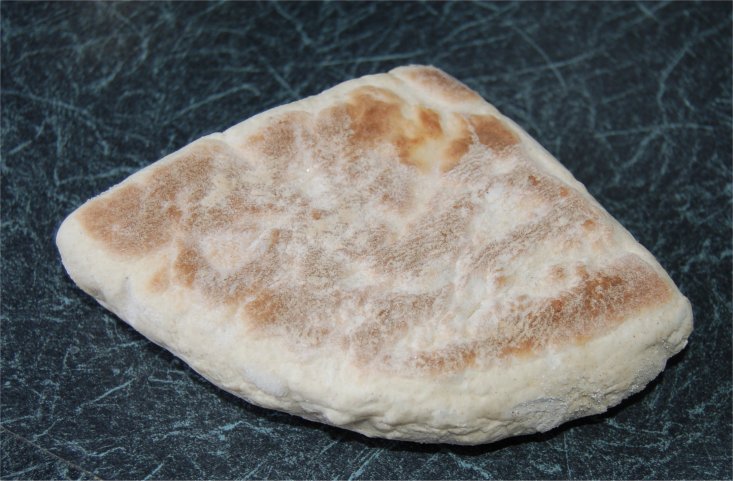 A single soda farl on a dark countertop, showing its pale floury crust with lightly browned griddle marks
