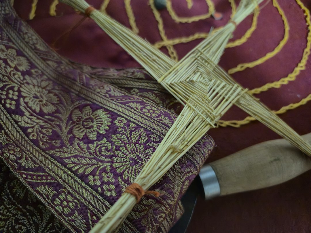 Hand-woven St. Brigid's Cross made from pale rushes, with a woven central square and four arms, lying on maroon patterned fabric