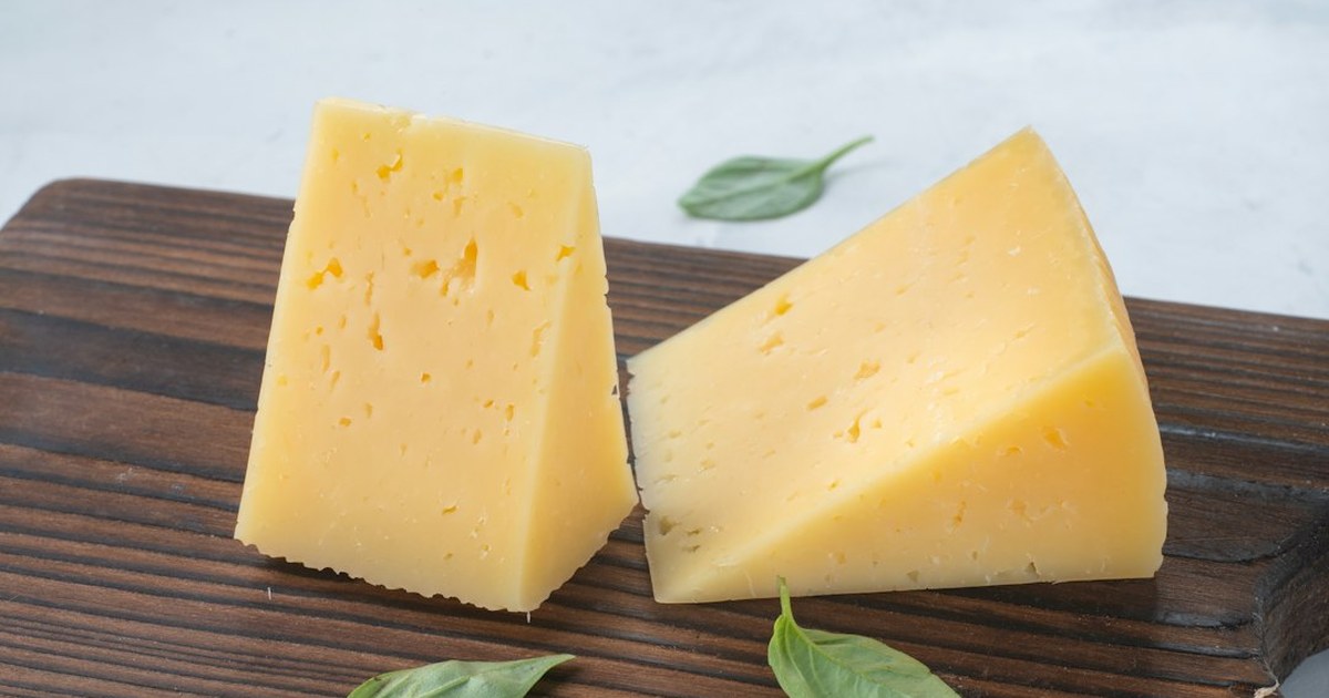 Wedges of aged farmhouse cheese with fresh basil on a wooden board