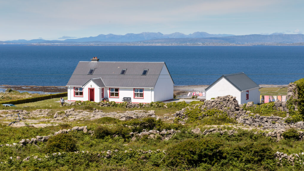 Whitewashed cottage with red-trimmed windows on Inishmore, Aran Islands, overlooking Galway Bay with the Connemara mountains in the distance