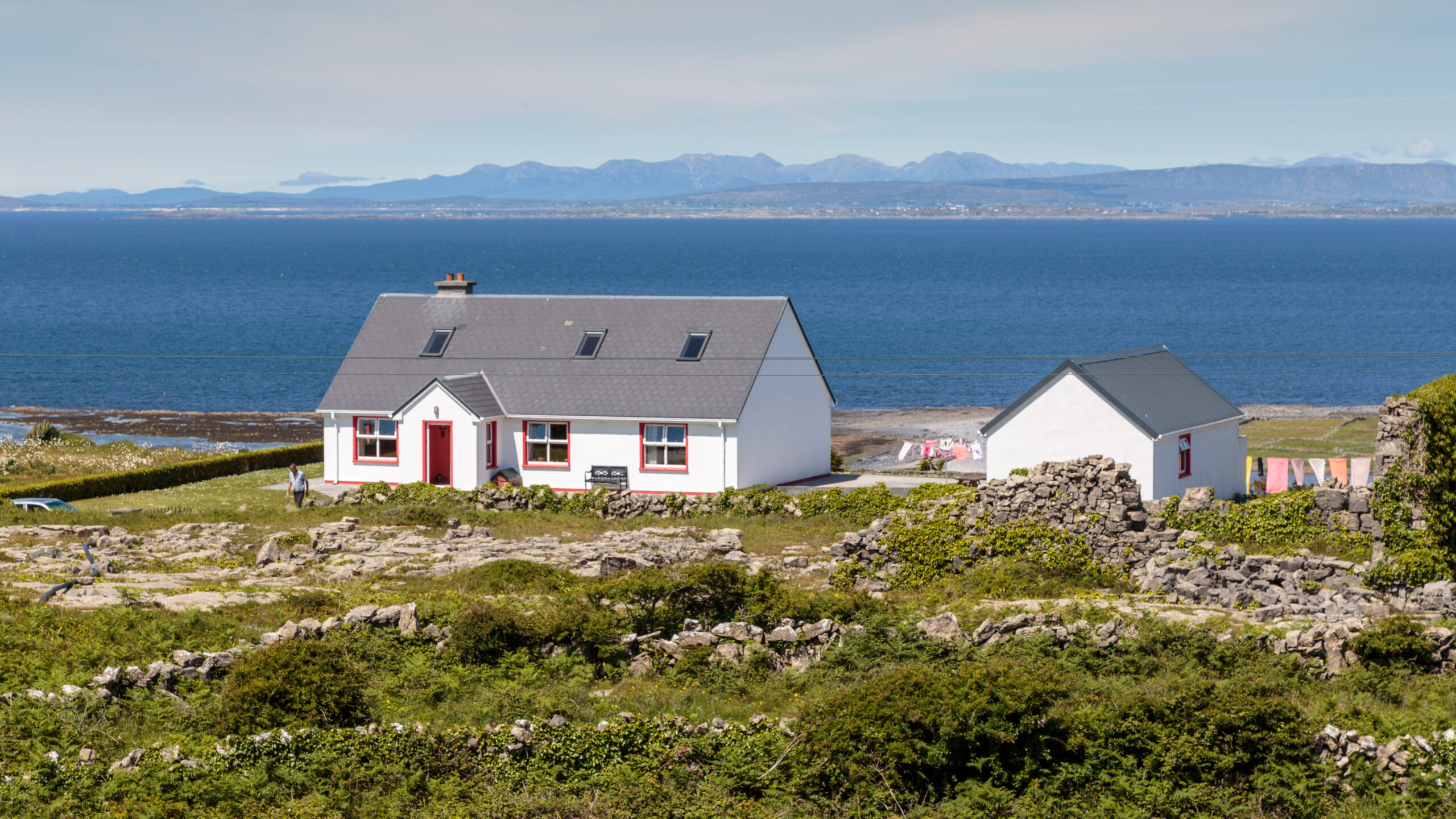 Whitewashed cottage with red-trimmed windows on Inishmore, Aran Islands, overlooking Galway Bay with the Connemara mountains in the distance