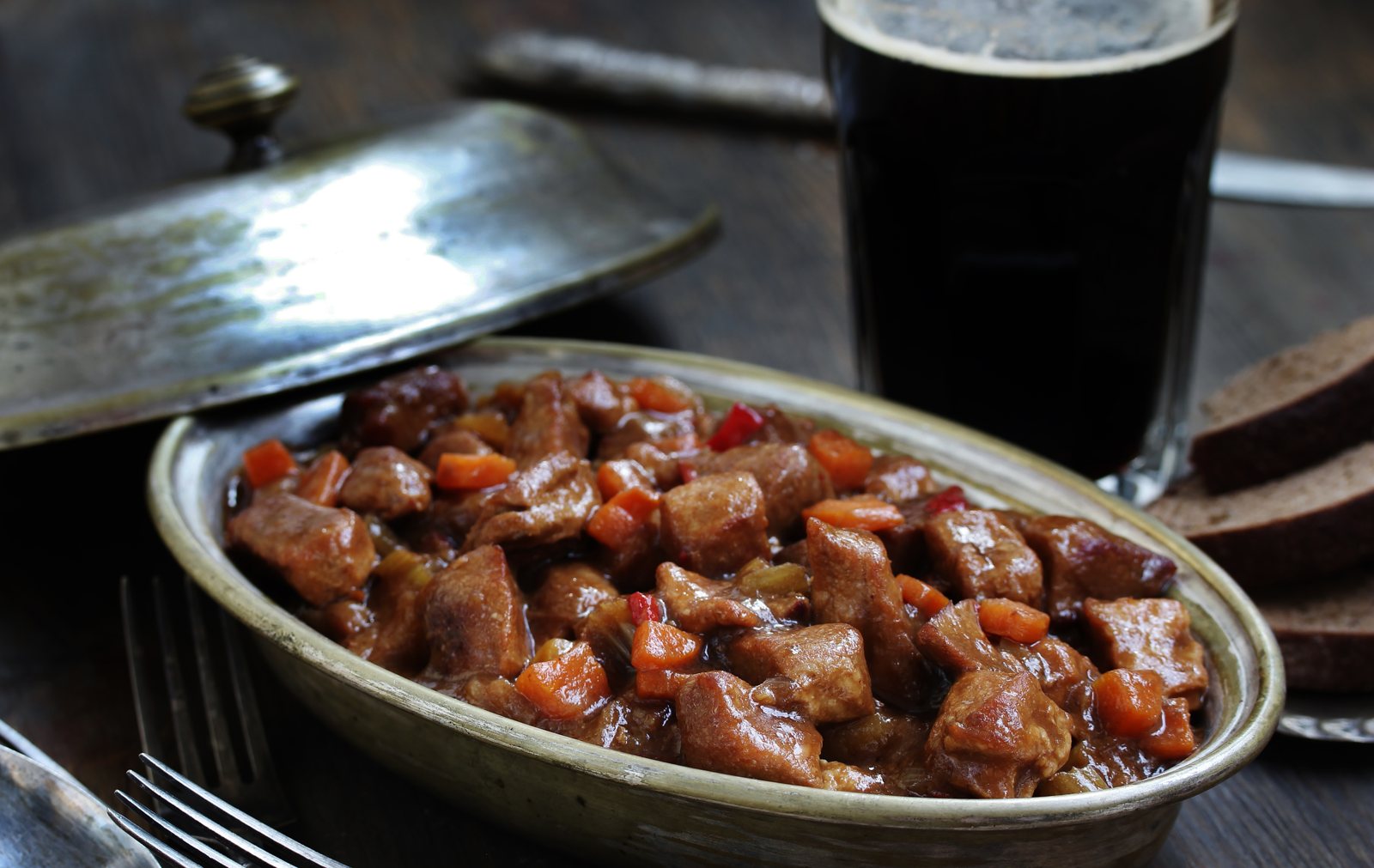 Beef and stout stew in an oval dish beside a pint of stout and slices of brown bread