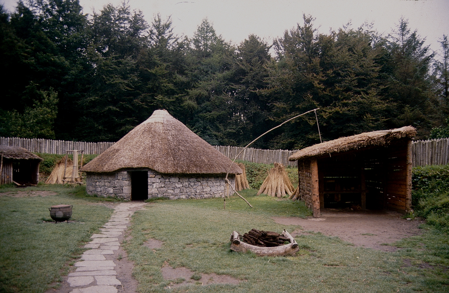 Reconstructed ringfort at Craggaunowen, County Clare — a thatched stone roundhouse inside a timber palisade, the kind of earthwork enclosure later reinterpreted in Irish folklore as a fairy fort