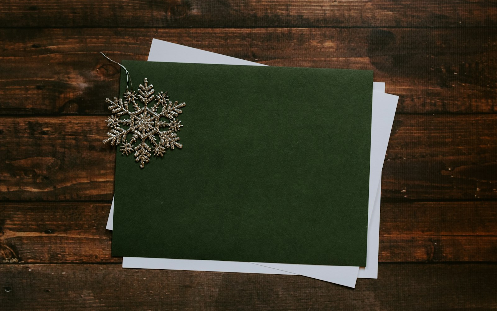 Blank dark green Christmas card with a glittering snowflake ornament on a wooden table, ready for a handwritten greeting