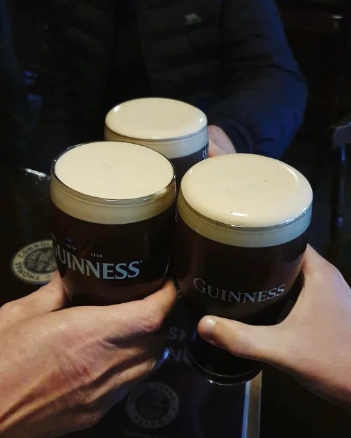 Three friends clinking pints of Guinness together in a dimly lit Irish pub