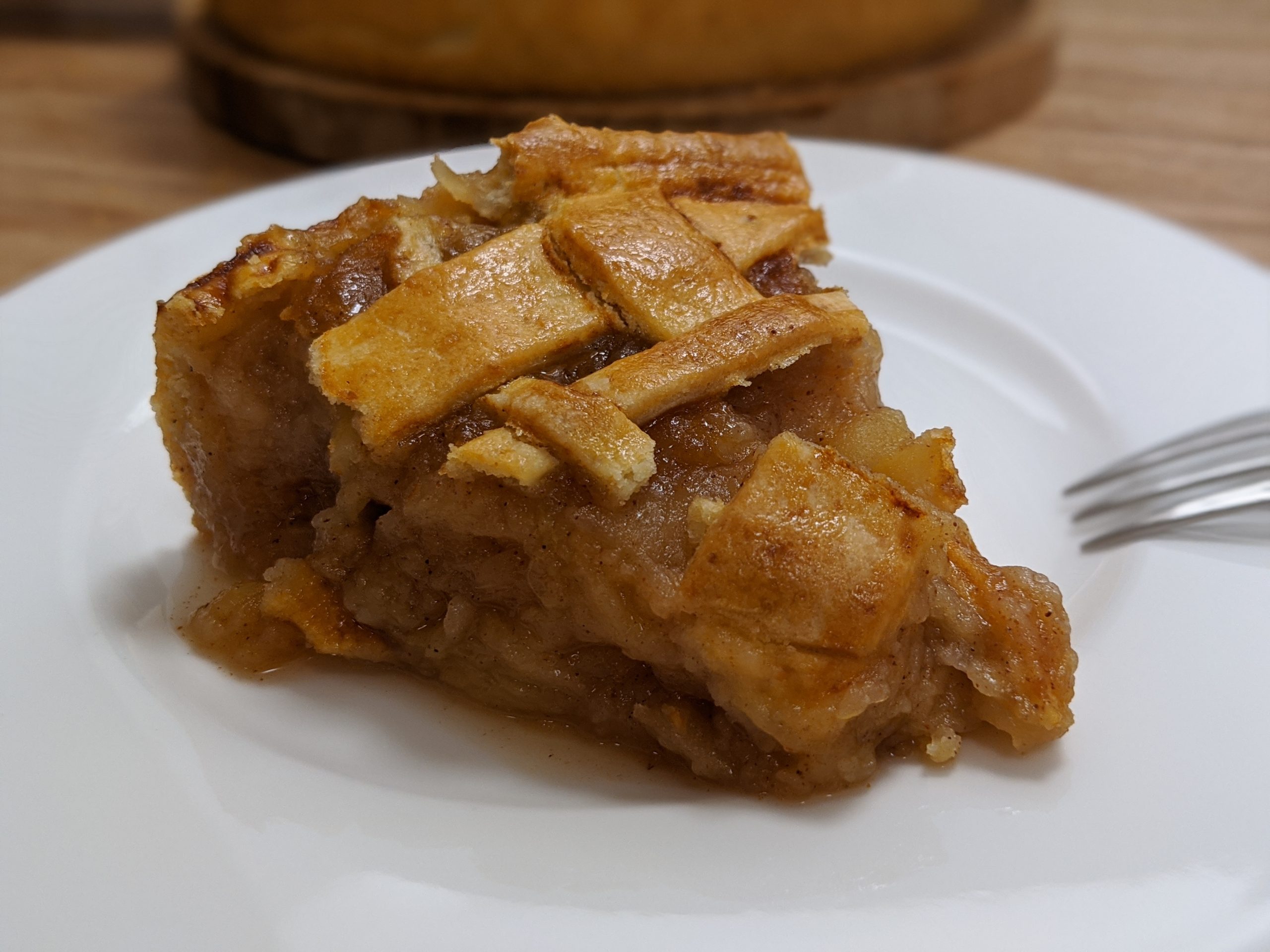 A wedge of golden lattice-topped Irish apple tart with tender spiced apple filling, served on a white plate