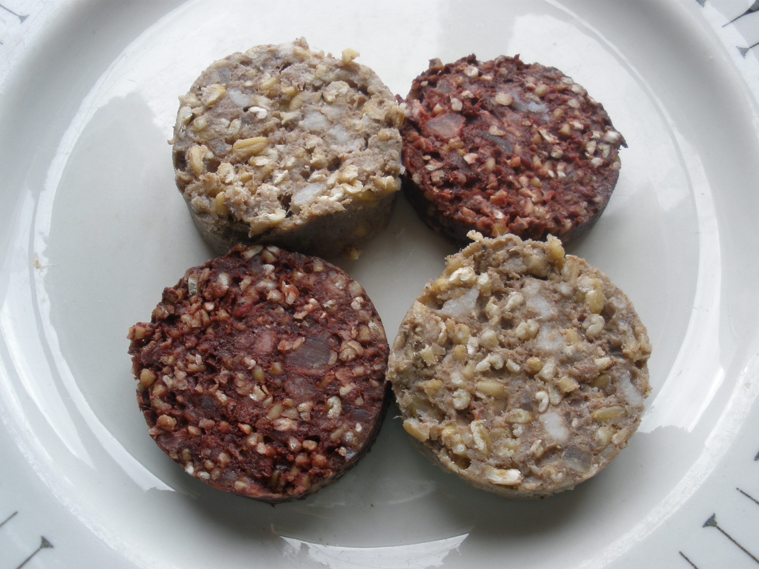 Raw sliced Irish black pudding and white pudding arranged on a plate, showing the texture before pan-frying