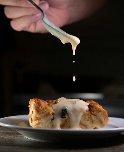 Slice of bread pudding with raisins, with warm custard being poured over it