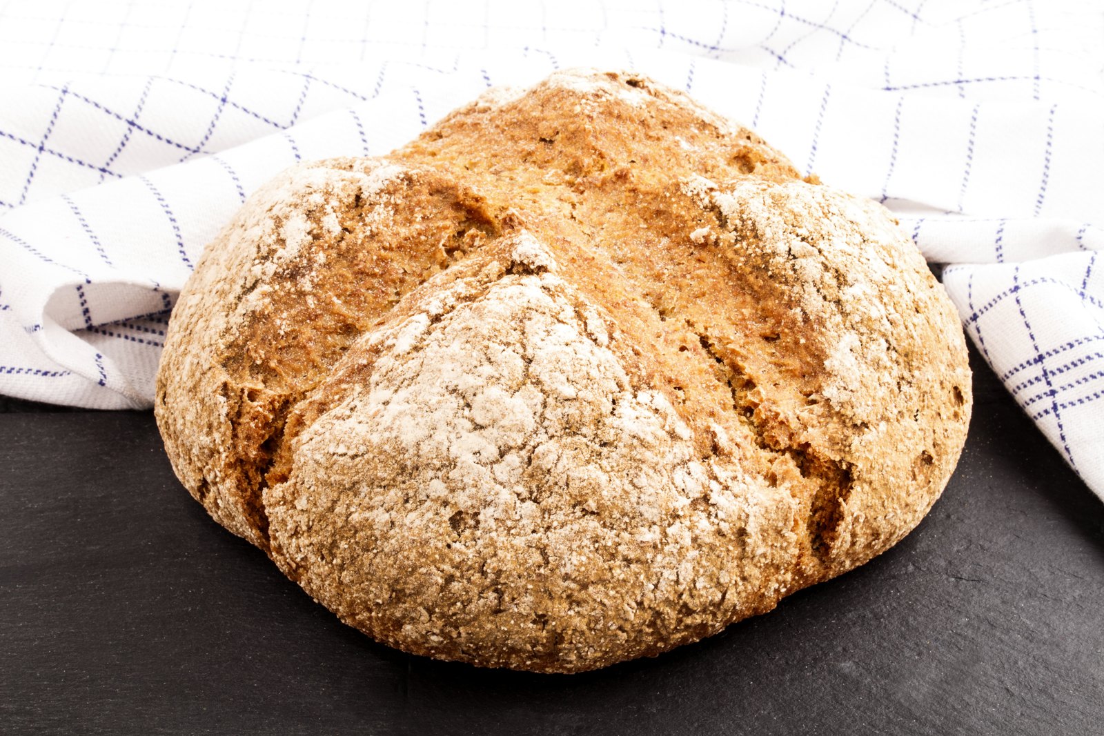 A round brown Irish soda bread loaf with a deep cross cut in the top, on a slate board