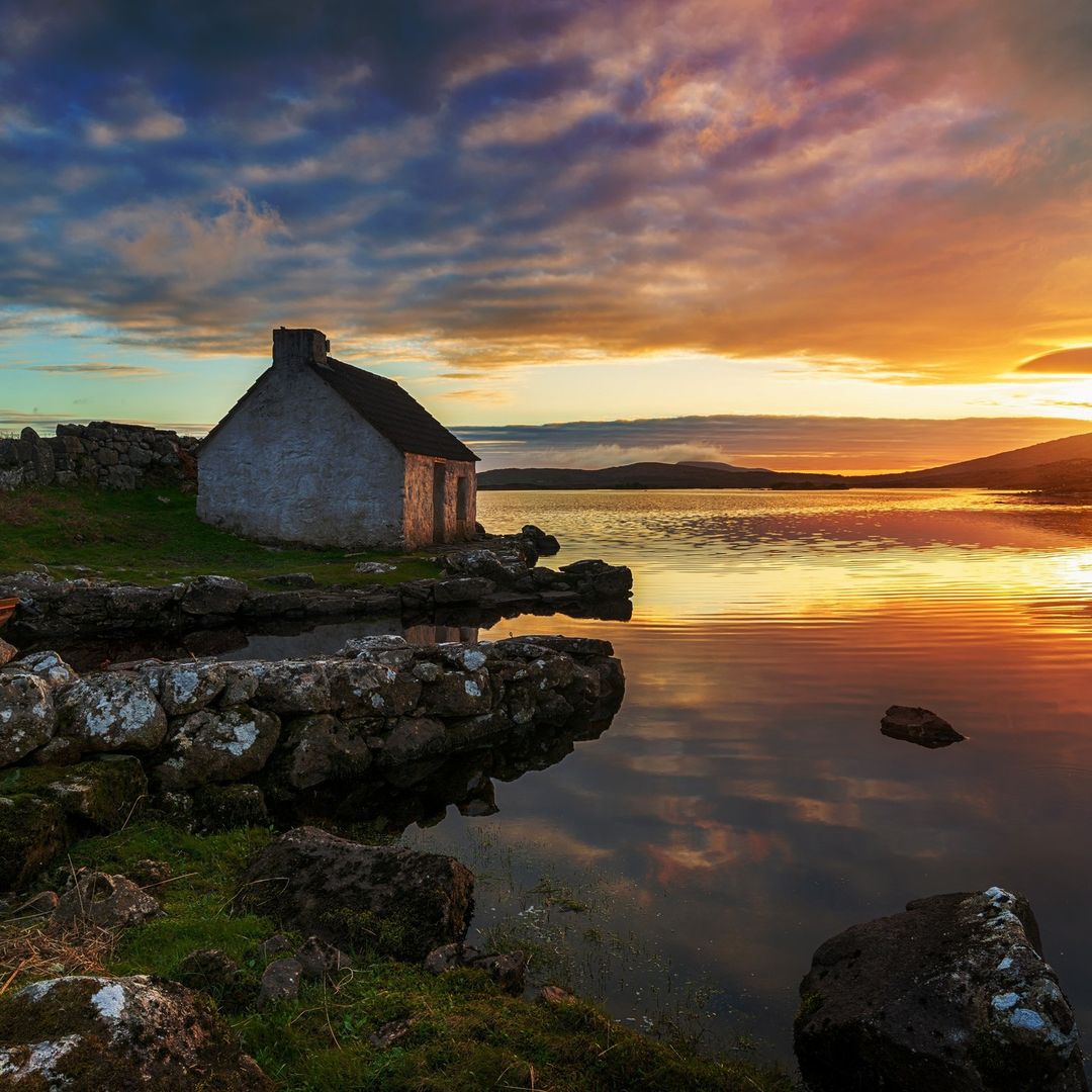 White stone cottage beside a calm lake in Connemara at sunset