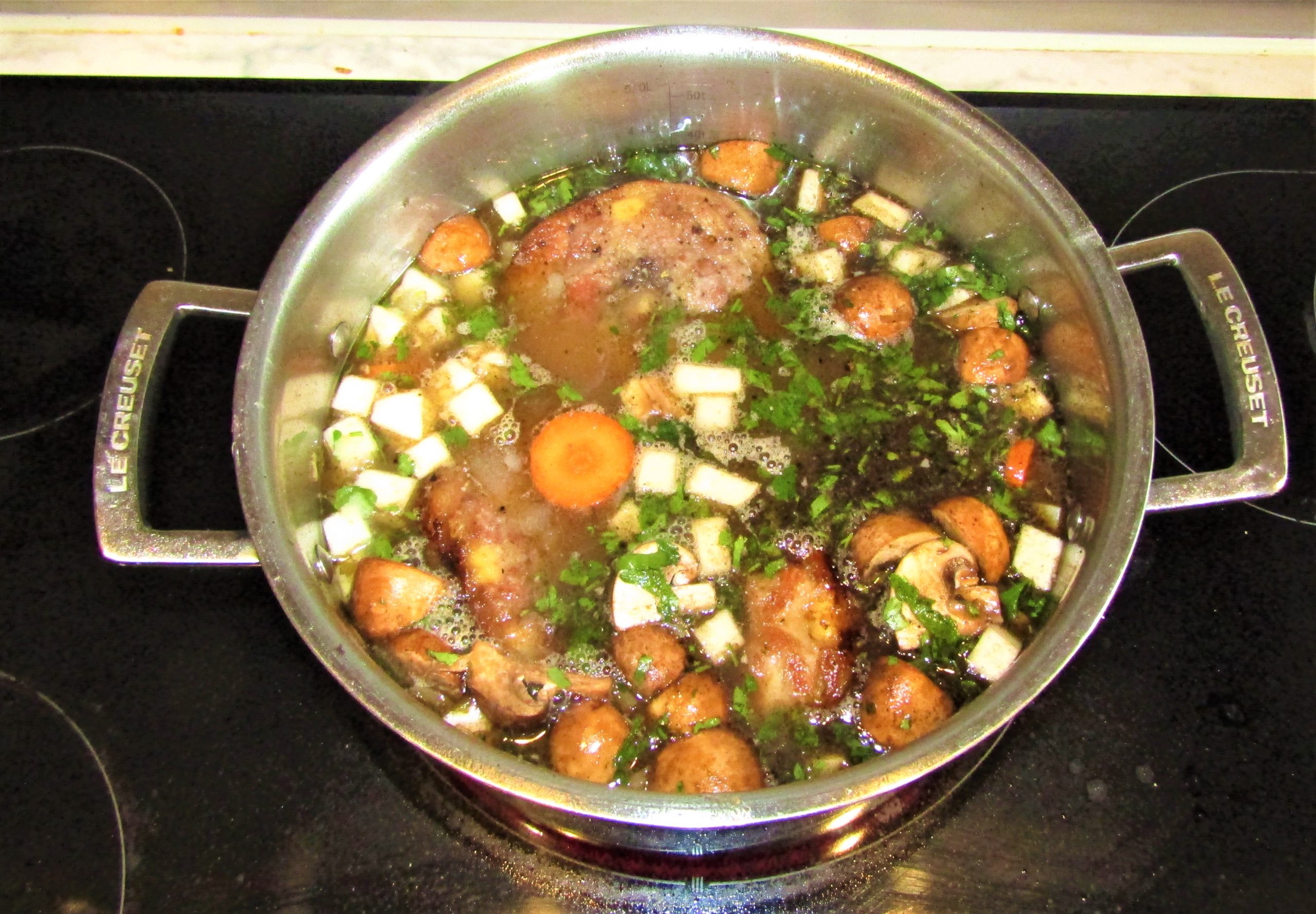 A pot of Irish stew simmering with chunks of meat, mushrooms, diced root vegetables and fresh parsley