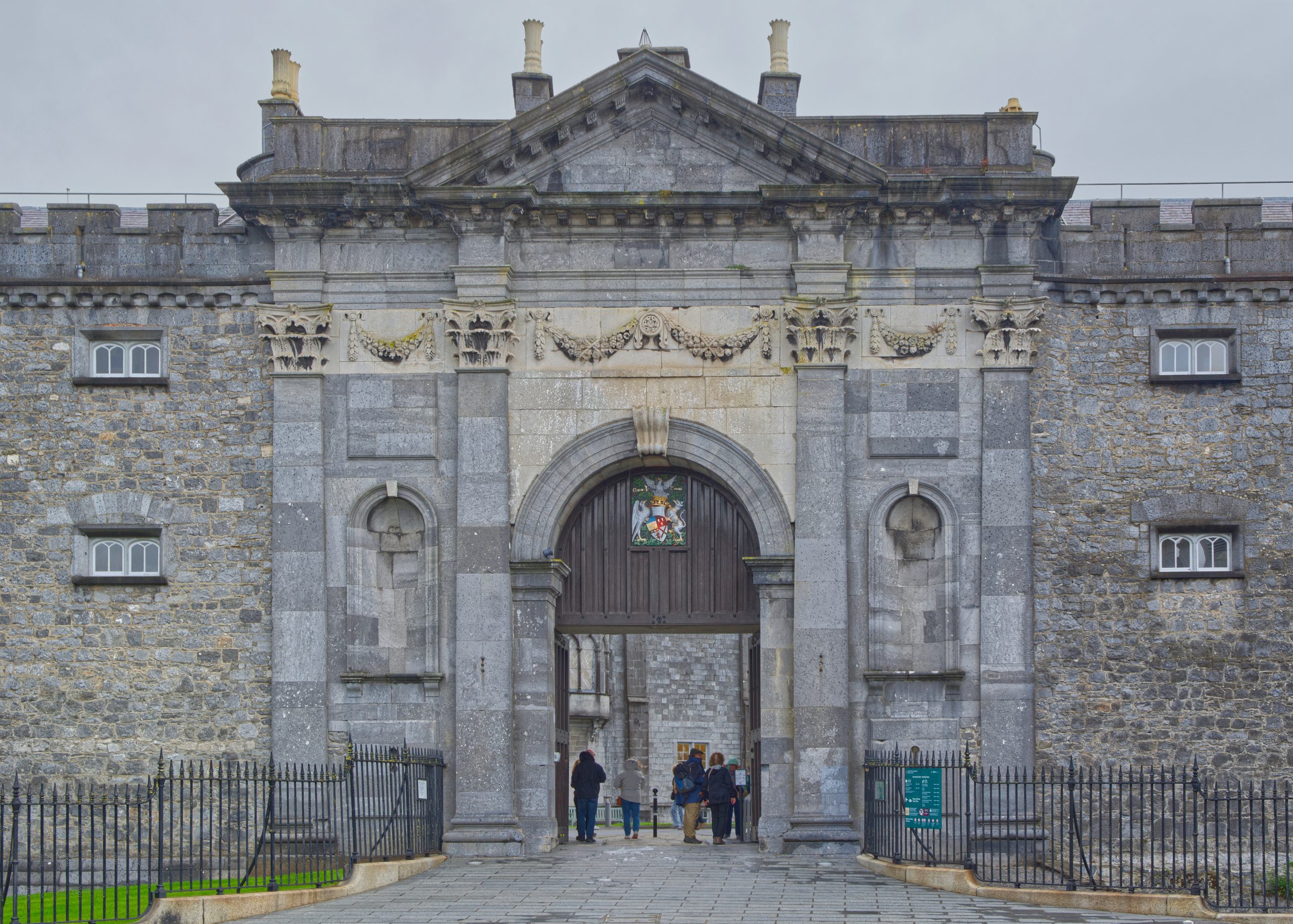Stone gatehouse of Kilkenny Castle with classical carved stonework and a wooden door, with visitors at the entrance