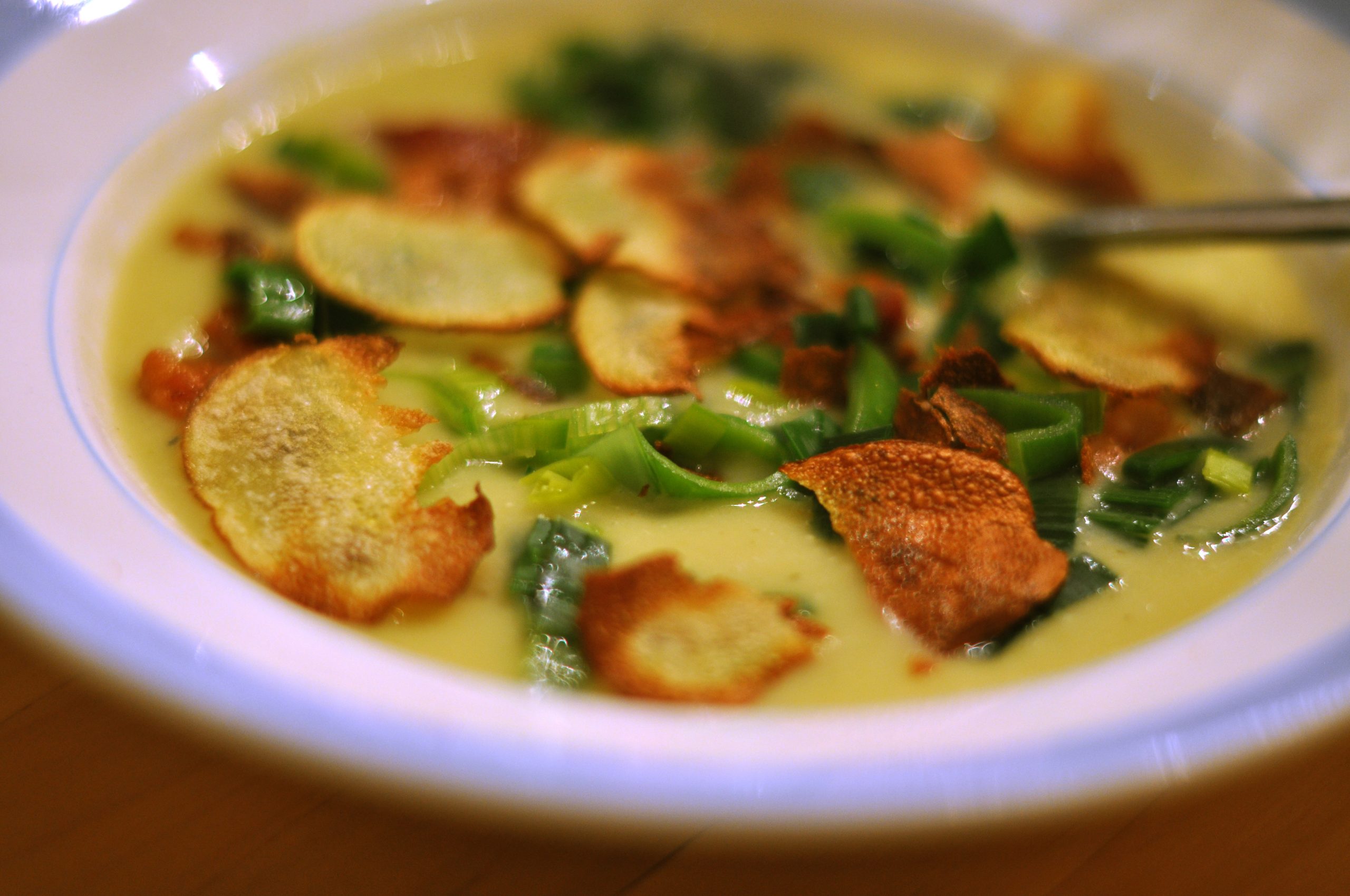 Creamy potato soup topped with crispy fried potato crisps, bacon pieces, and chopped spring onion