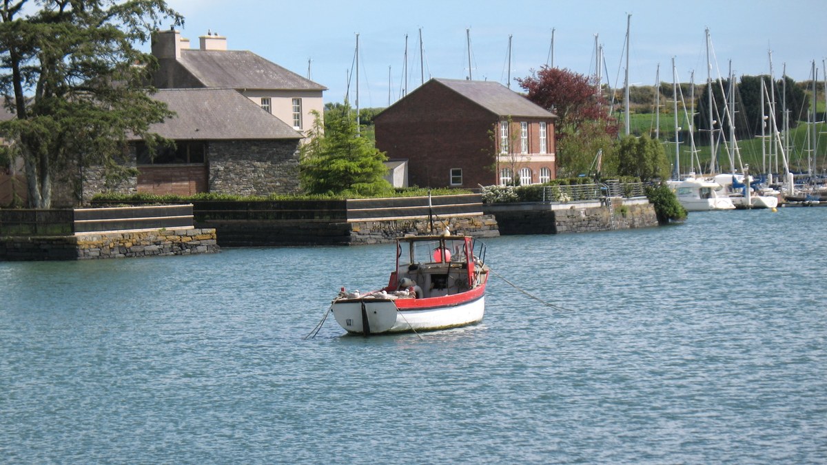 A small fishing boat moored in Kinsale harbour, County Cork, with stone houses and yachts behind