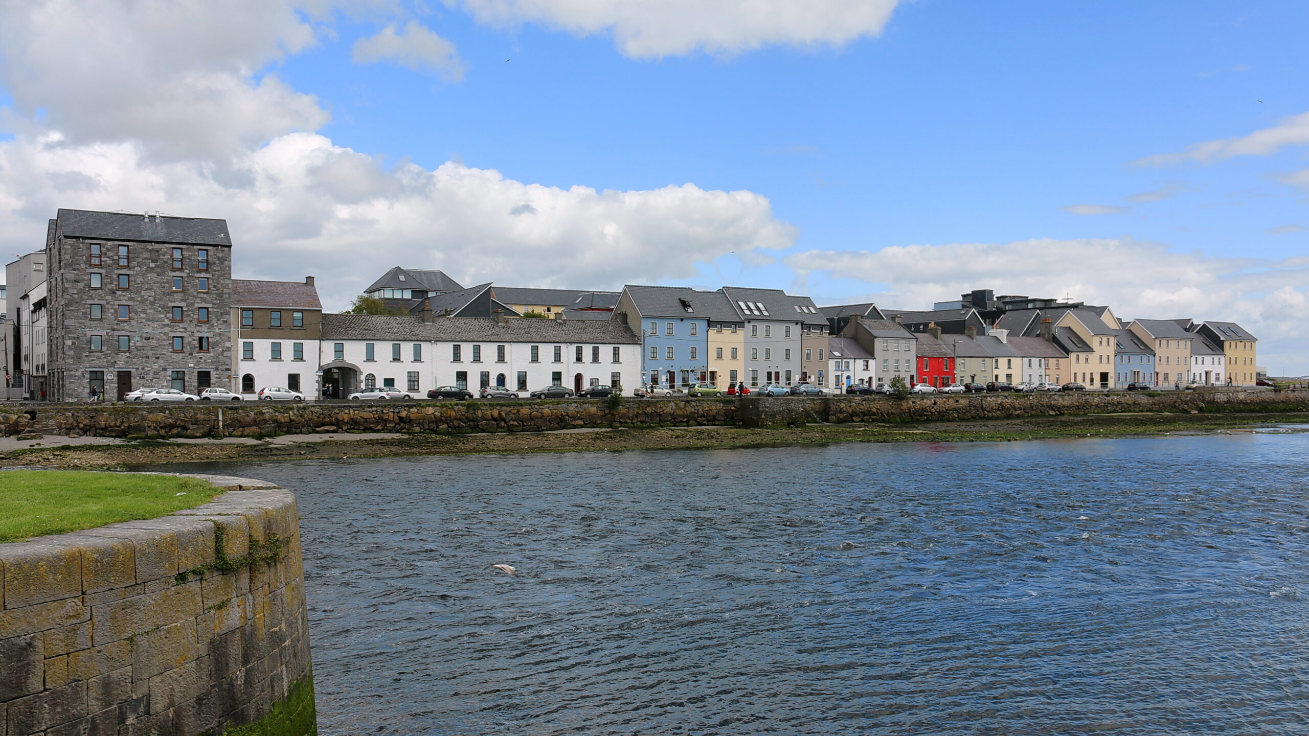 Colourful painted houses along the Long Walk quay on the River Corrib in Galway, including a bright red house, seen from across the water on a sunny day