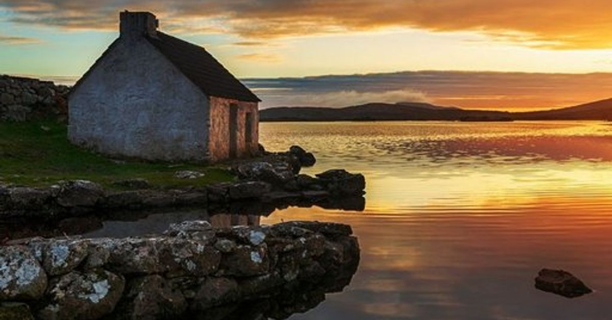 Traditional Irish stone cottage at sunset beside a Connemara lake, with stone chimney